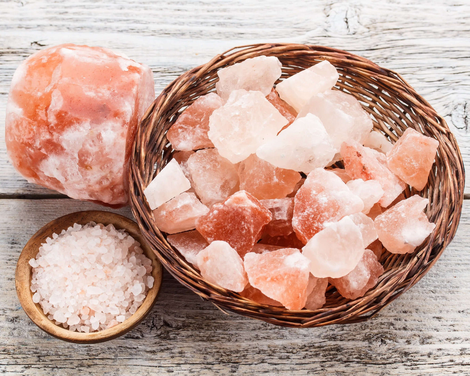 Himalayan pink salt rocks in a wicker basket with a small wooden bowl of salt on a wooden surface.